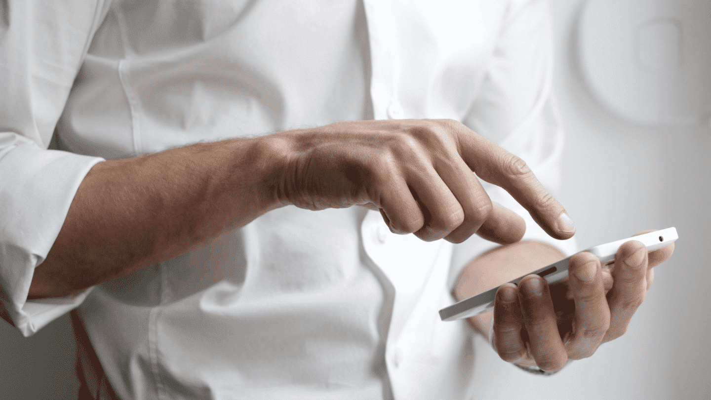 Homme en chemise blanche qui pianote sur l'écran d'un smartphone