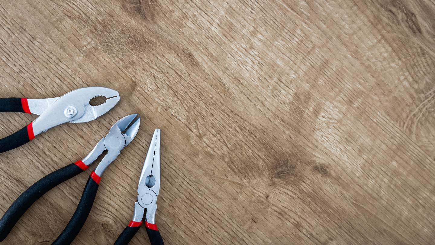 Trois pinces à manches noirs et rouges posées sur un plan de travail en bois