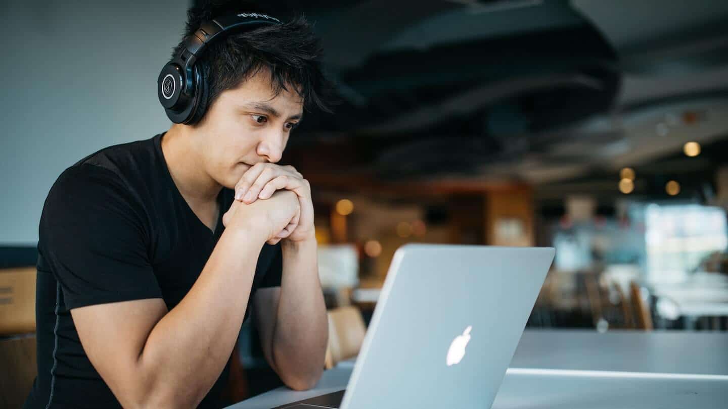 Homme au casque audio, mains jointes sous le menton, concentré devant un ordinateur portable